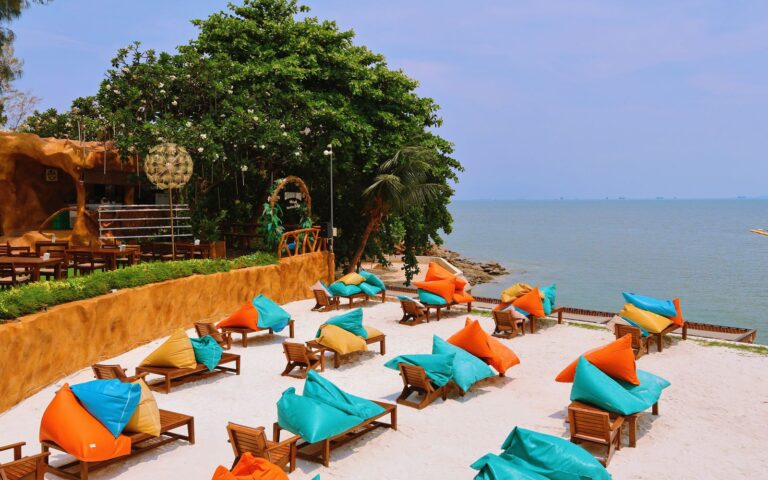 Vibrant beach scene in Thailand with colorful loungers, turquoise sea, and green foliage, perfect for relaxation