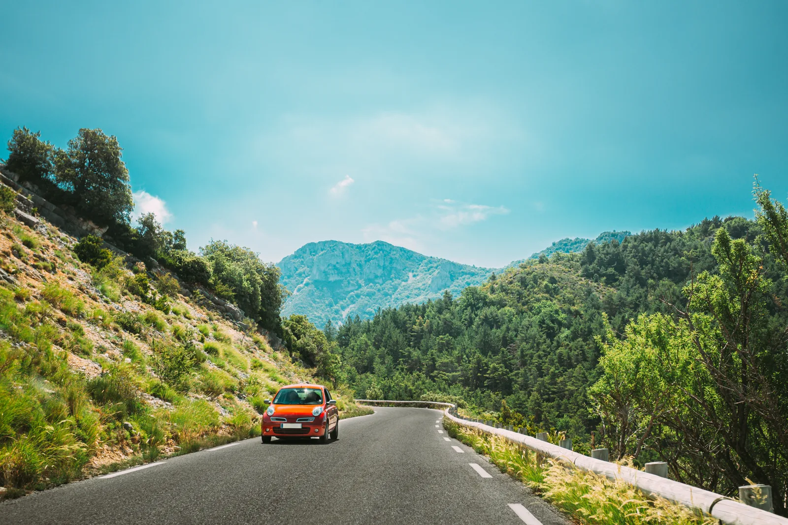 Red car driving on a winding mountain road in Provence, France