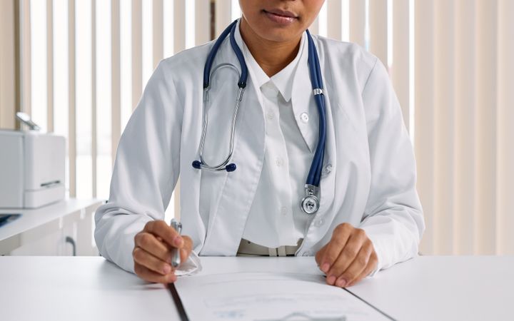 Doctor with a stethoscope writing notes at a clinic desk