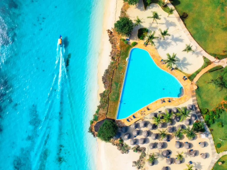 Aerial view of a beach resort pool, palm trees and blue sea