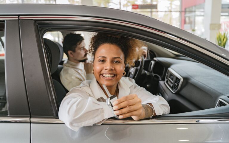 Joyful couple in their new car, holding keys in a dealership showroom, smiling warmly